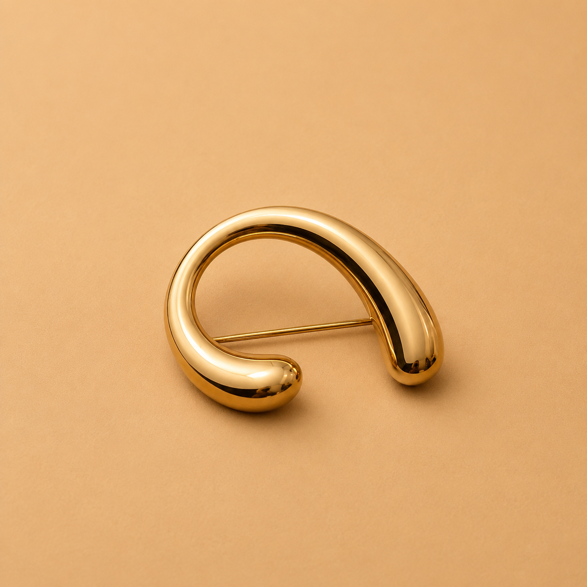A polished gold crescent-shaped brooch with a pin mechanism, displayed on a warm beige background.