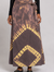 Woman wearing a brown and yellow tie-dye wrap maxi skirt with a side tie waist and black leather slide sandals.
